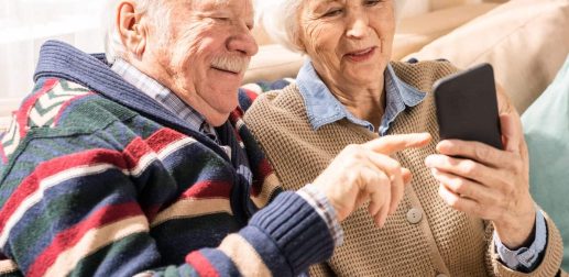 Portrait of adorable senior couple using smartphone together video chatting with family at home, copy space